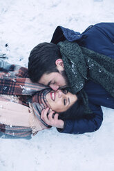 Hoher Blickwinkel des Mannes, der seine Freundin küsst, während er auf einem schneebedeckten Feld liegt - CAVF45242