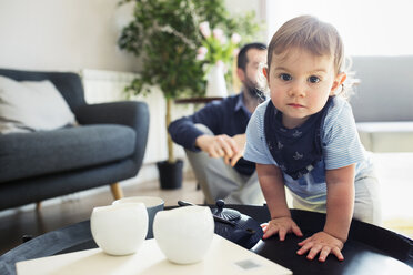 Porträt eines kleinen Jungen, der zu Hause am Tisch steht, mit seinem Vater im Hintergrund - CAVF45244