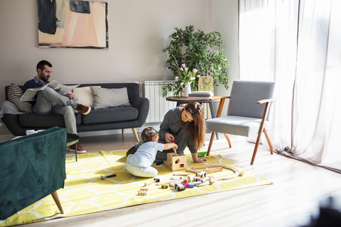 Mann liest Zeitung, während die Mutter mit ihrem Sohn zu Hause spielt, lizenzfreies Stockfoto