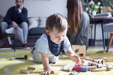 Junge spielt mit Spielzeugeisenbahn, Eltern im Hintergrund - CAVF45249