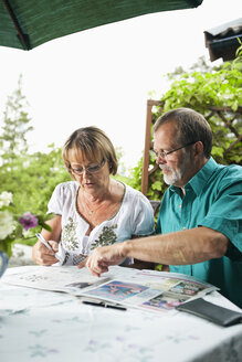 Älteres Paar sitzt im Hinterhof des Hauses und liest Zeitung - MASF06483