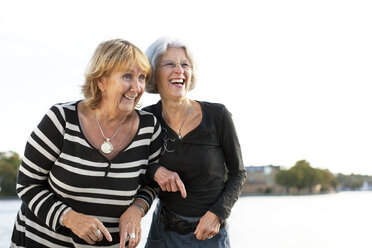 Retired female friends looking at something and laughing outdoors - MASF06485