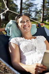 Smiling woman relaxing on hammock with book - MASF06487