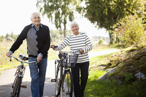 Älteres Paar geht mit Fahrrädern im Park spazieren - MASF06493
