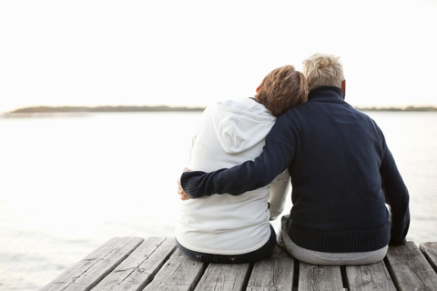 Rückansicht eines reifen Paares, das auf einem Steg sitzt und auf den See blickt, lizenzfreies Stockfoto