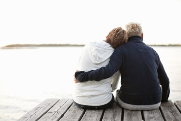 Rückansicht eines reifen Paares, das auf einem Steg sitzt und auf den See blickt - MASF06498