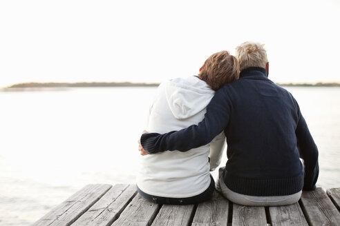 Rear view of mature couple sitting on pier looking at lake - MASF06498