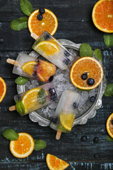 Hausgemachtes Detox-Eis mit Heidelbeeren, Orangenscheiben und Minzblättern auf schwarzem Holz - RTBF01165