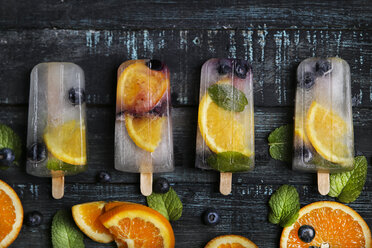Hausgemachtes Detox-Eis mit Heidelbeeren, Orangenscheiben und Minzblättern auf schwarzem Holz - RTBF01166