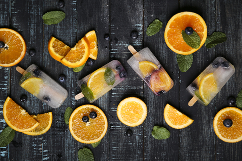 Homemade detox popsicles with blueberries, orange slices and mint leaves on black wood stock photo