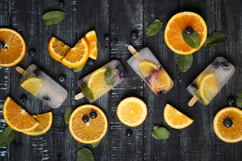 Hausgemachtes Detox-Eis mit Heidelbeeren, Orangenscheiben und Minzblättern auf schwarzem Holz - RTBF01167