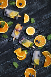 Hausgemachtes Detox-Eis mit Heidelbeeren, Orangenscheiben und Minzblättern auf schwarzem Holz - RTBF01168