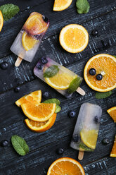 Homemade detox popsicles with blueberries, orange slices and mint leaves on black wood - RTBF01169