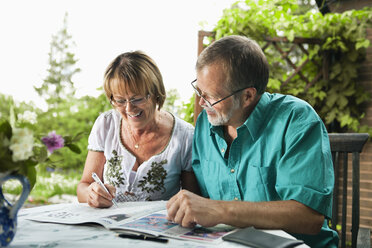 Happy senior couple solving crossword in newspaper together - MASF06551