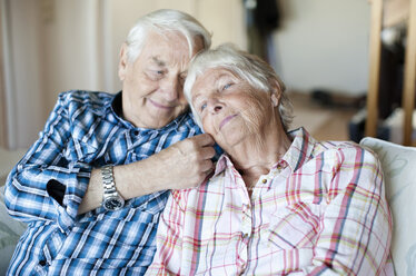 Loving senior man with wife sitting on sofa in living room - MASF06556