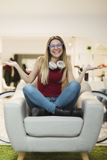 Happy casual young woman sitting in armchair in coworking space - OCAF00217