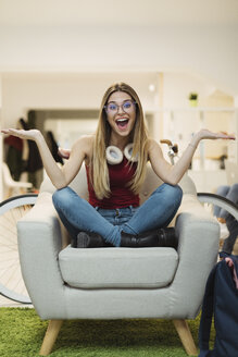 Glückliche junge Frau, die in einem Sessel im Coworking Space sitzt - OCAF00219