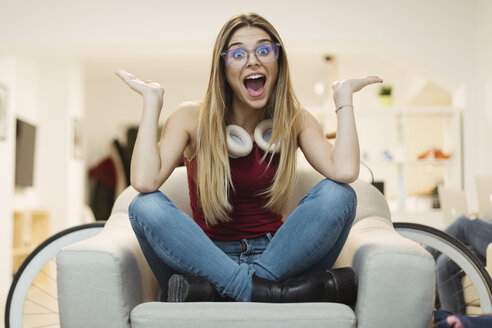 Glückliche junge Frau, die in einem Sessel im Coworking Space sitzt - OCAF00220