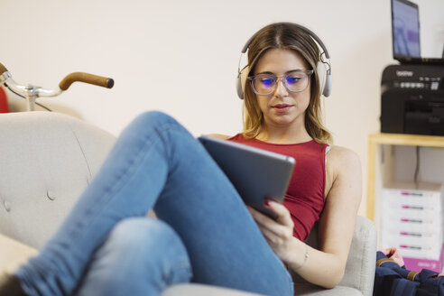 Lässige junge Frau mit Kopfhörern und Tablet in einem Coworking Space - OCAF00221