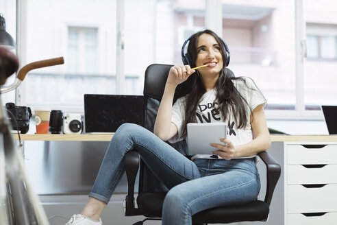 Lässige junge Frau mit Notizblock und Kopfhörern im Coworking Space - OCAF00223