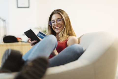 Glückliche junge Frau mit Smartphone und Kreditkarte im Büro, lizenzfreies Stockfoto