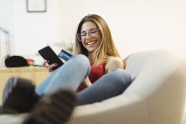 Happy young woman using smartphone and credit card in the office - OCAF00228