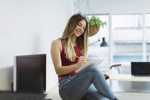 Smiling casual young woman taking notes in the office - OCAF00231