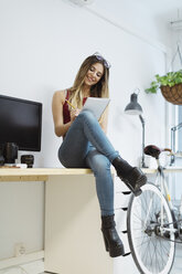 Lächelnde, lässige junge Frau, die am Schreibtisch im Büro sitzt und Notizen macht - OCAF00232