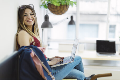 Smiling casual young woman using laptop in the office - OCAF00235