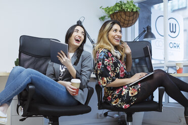 Zwei glückliche junge Frauen im Büro mit Laptop und Tablet - OCAF00238