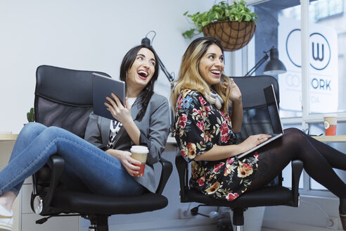 Zwei glückliche junge Frauen im Büro mit Laptop und Tablet - OCAF00238