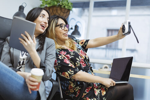 Zwei glückliche junge Frauen im Büro machen ein Selfie - OCAF00239