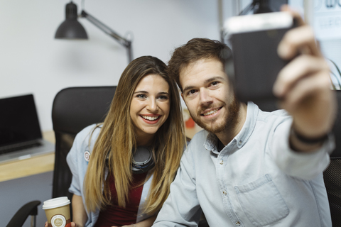 Zwei lächelnde Arbeitskollegen im Büro machen ein Selfie, lizenzfreies Stockfoto