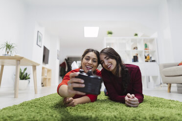 Zwei glückliche junge Frauen, die in einem Coworking Space auf dem Boden liegen und ein Selfie machen - OCAF00245