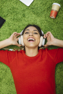 Happy young woman lying on carpet listening to music with headphones - OCAF00246