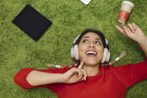 Happy young woman lying on carpet listening to music with headphones stock photo