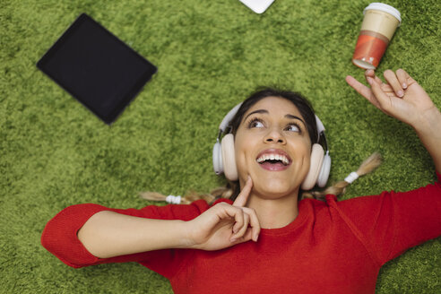 Glückliche junge Frau, die auf einem Teppich liegt und mit Kopfhörern Musik hört - OCAF00247