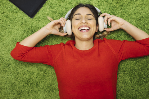 Happy young woman lying on carpet listening to music with headphones stock photo