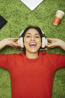Glückliche junge Frau, die auf einem Teppich liegt und mit Kopfhörern Musik hört - OCAF00249