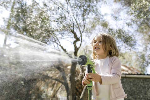 Smiling little girl playing with garden hose stock photo