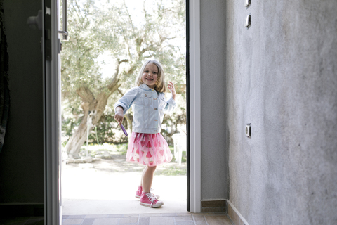 Portrait of laughing little girl standing in front of open entry door stock photo