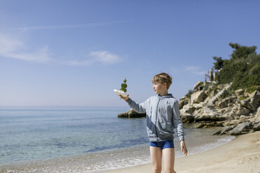 Boy standing on the beach with self-made toy boat - KMKF00218