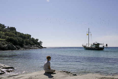 Junge sitzt am Meer und betrachtet die Aussicht, lizenzfreies Stockfoto