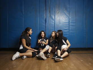 Glückliche Mädchen sitzen auf dem Holzboden eines Volleyballfeldes - CAVF45259