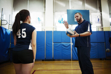 Männlicher Trainer erklärt jugendliches Mädchen im Volleyballfeld - CAVF45275
