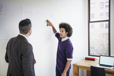 Businessman explaining chart to colleague while standing in creative office - CAVF45319