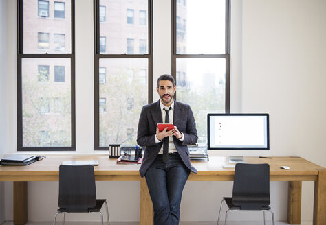 Porträt eines Geschäftsmannes, der einen Tablet-Computer benutzt und sich auf einen Schreibtisch im Büro stützt - CAVF45338
