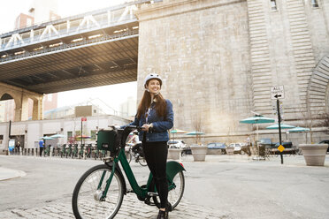 Frau mit Fahrrad auf Stadtstraße gegen Brücke - CAVF45351
