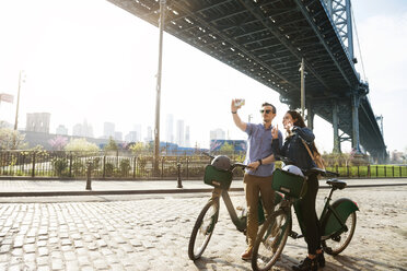 Paar, das ein Selfie macht, während es mit Fahrrädern vor der Manhattan-Brücke steht - CAVF45354