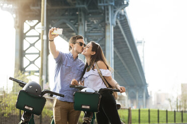 Couple kissing while taking selfie with bicycles against Manhattan Bridge - CAVF45357